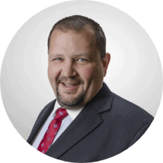 alt="Circle head shot of Matthias Allred, insurance advisor at Inside Insurance, wearing a black suit and a red necktie."